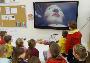 Dzieci oglądają na monitorze lalkę teatralną.